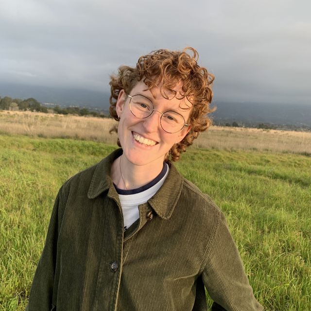 Katie in a olive green shirt smiling in a field of green and tan grasses.