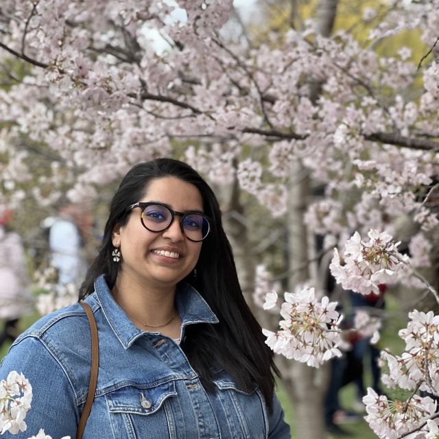 Paavani stands in front of a pink blossoming tree wearing a demin jacket.