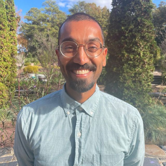 Mook stands in front of trees smiling at the camera.